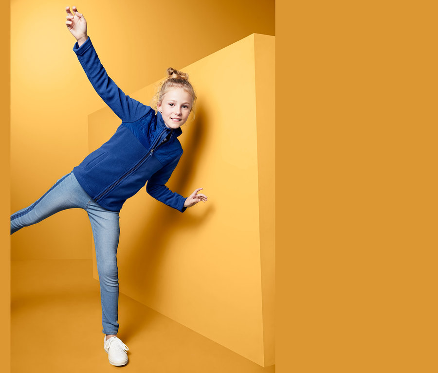 Dievča pózuje v hybridnej flísovej bunde na žltom pozadí.