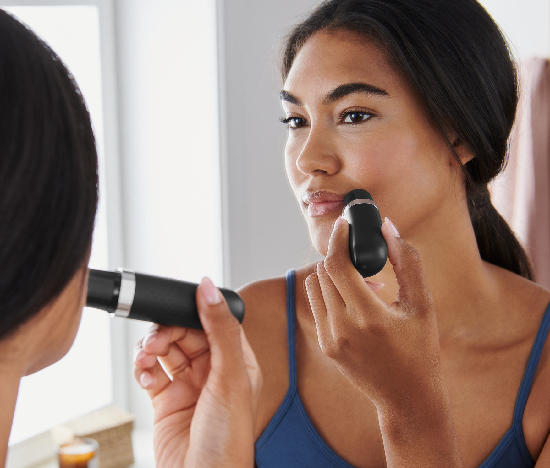 Žena používa elektrický depilátor na tvár pred zrkadlom.