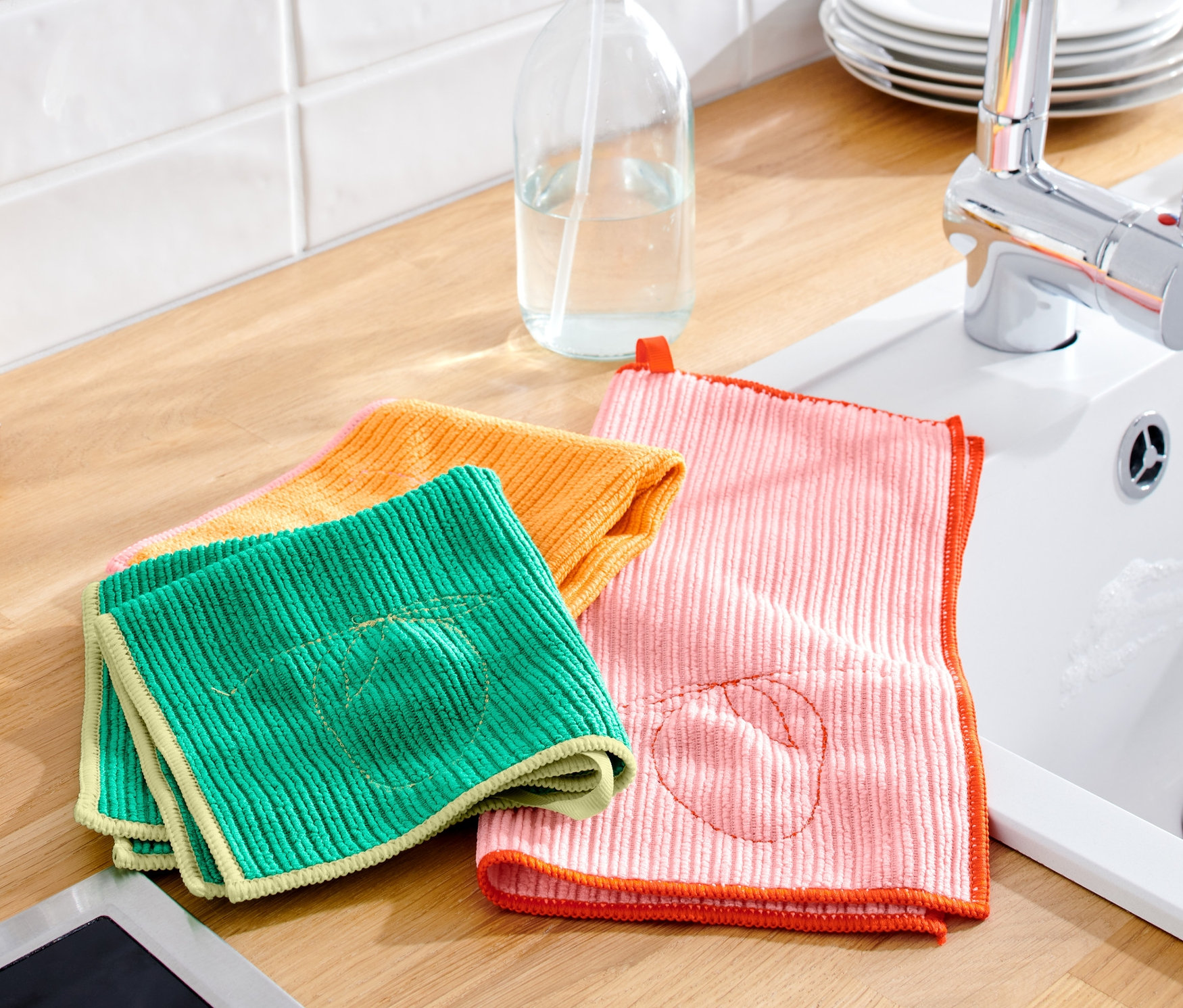 Na linke ležia zelená, oranžová a ružová univerzálne čistiace handričky, 3 ks, vedľa drezu a fliaš s olejom.