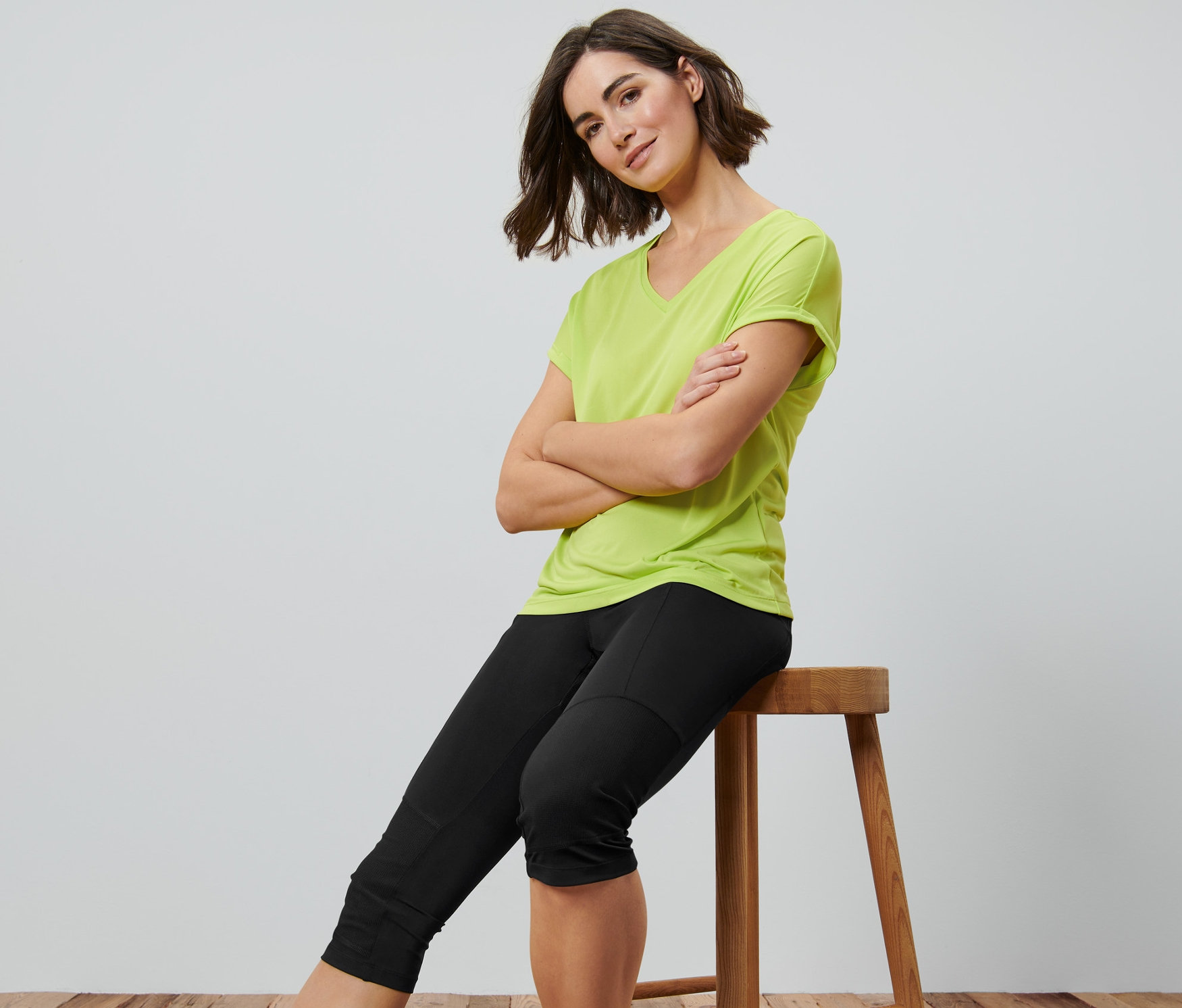 Žena sedí na stoličke s prekríženými rukami a má na sebe čierne 3/4 trekingové legínsy.