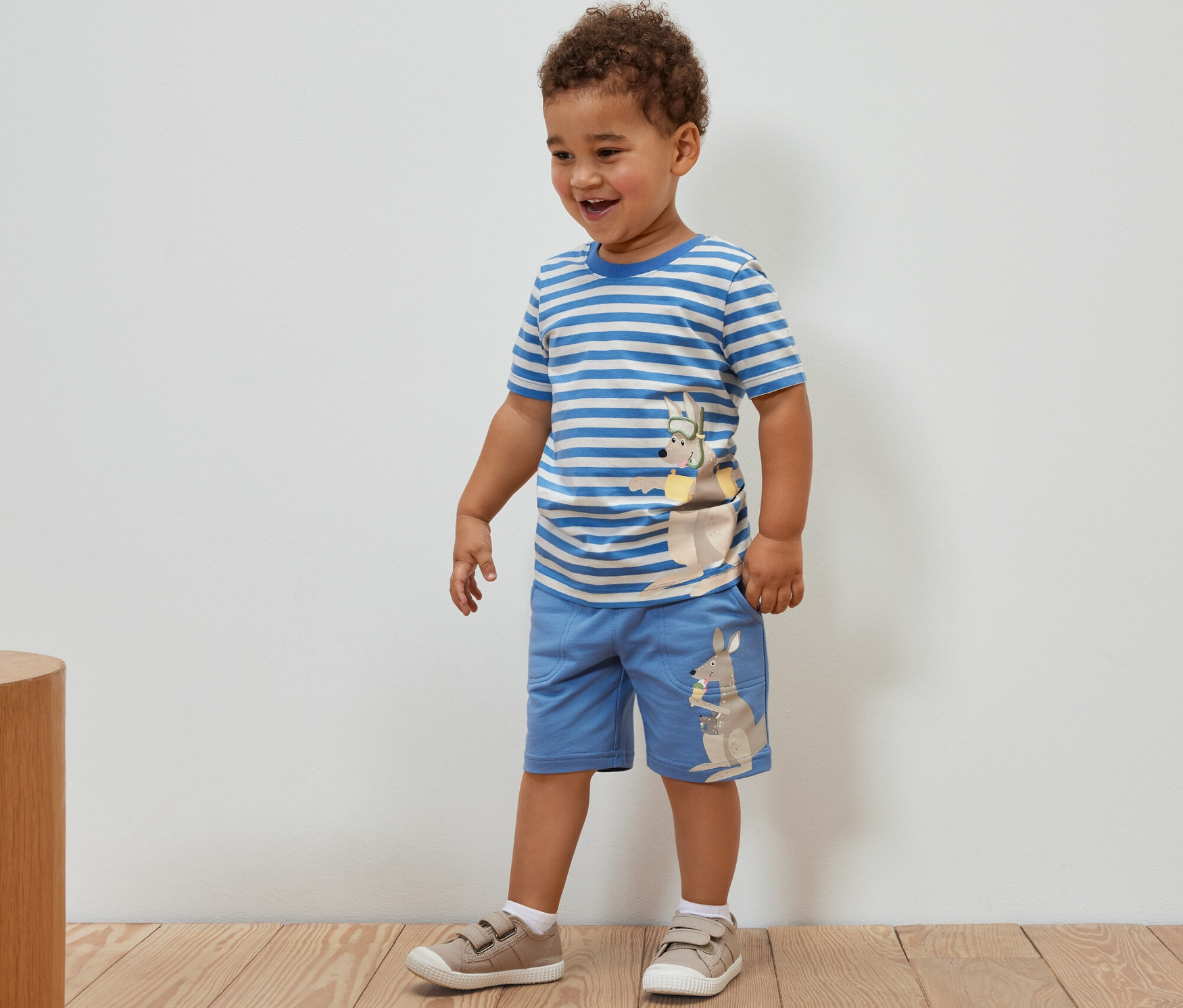 Chlapec stojí a má na sebe detské tričká s aplikáciou, 2 ks a šortky s aplikáciou klokana.