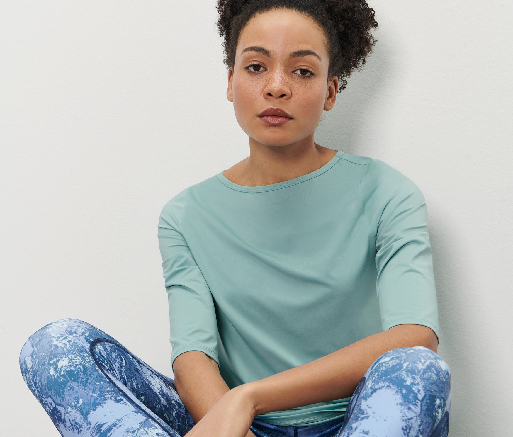 Žena sedí a má na sebe mätové funkčné tričko s 3/4 rukávmi.