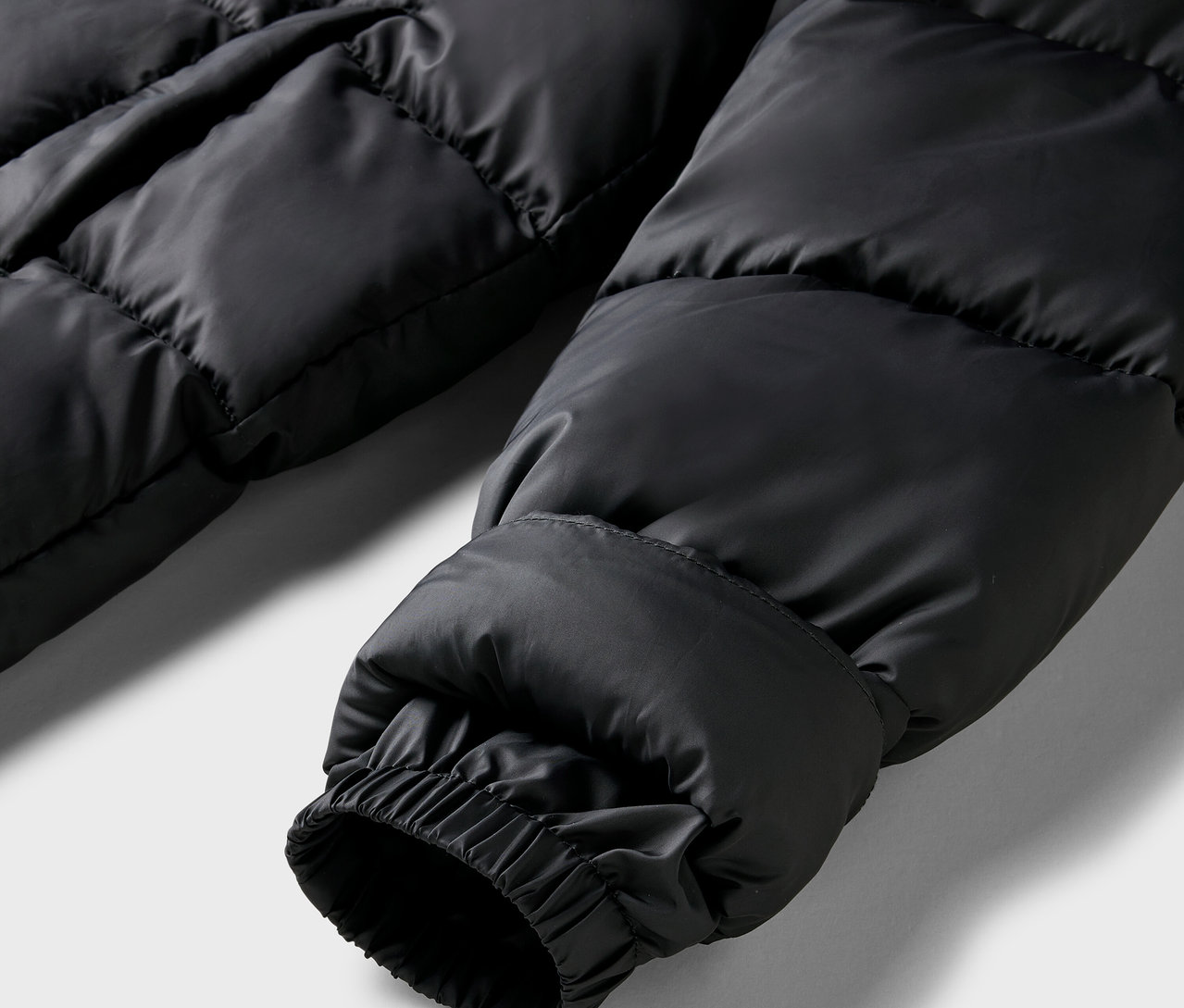 Detail čiernej prešívanej bundy s elastickou manžetou.