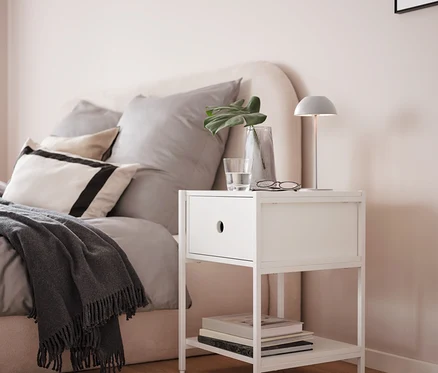 Sivá stolová LED lampa s akumulátorom na bielom nočnom stolíku vedľa postele.