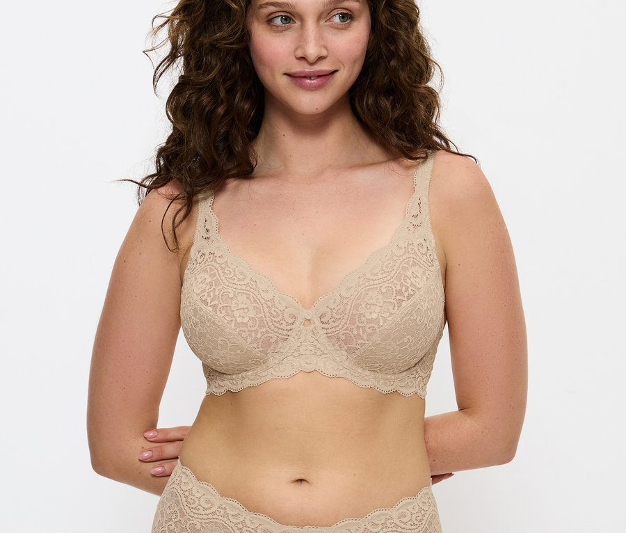 Žena s hnedými vlasmi pózuje v béžovej čipkovanej podprsenke a nohavičkách.