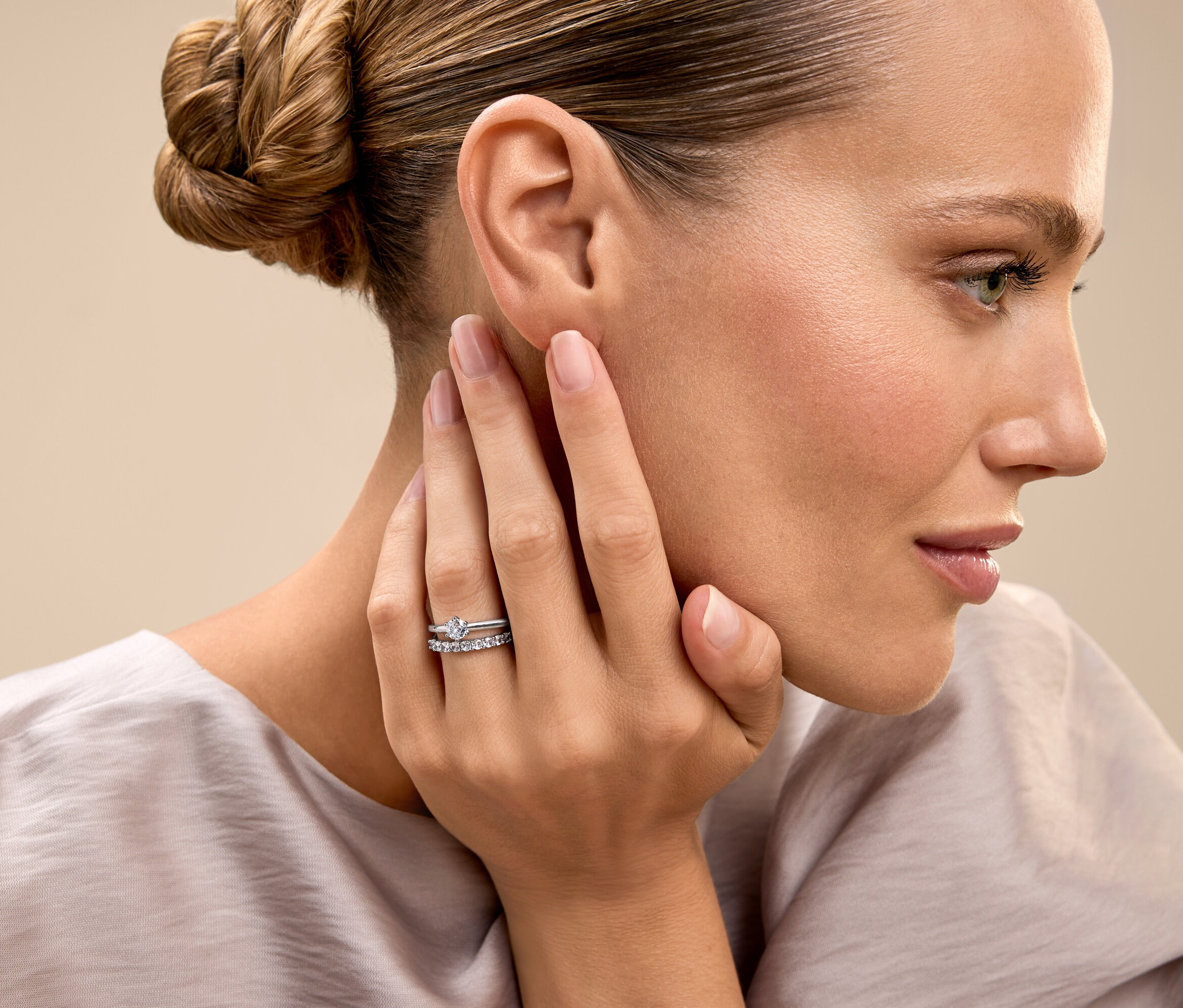 Žena so zopnutými vlasmi sa dotýka tváre a ukazuje prsteň.