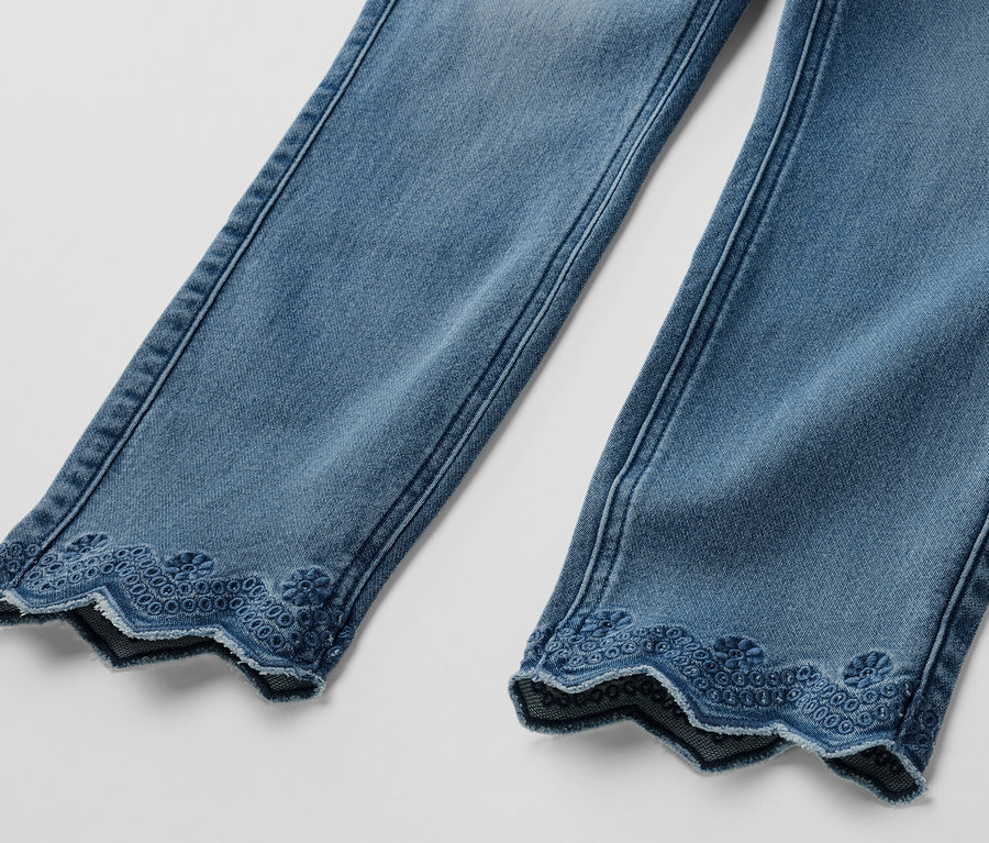 Detail dvoch nohavíc svetlomodrých sedemosminových tregínsov s ažúrovou výšivkou na leme.