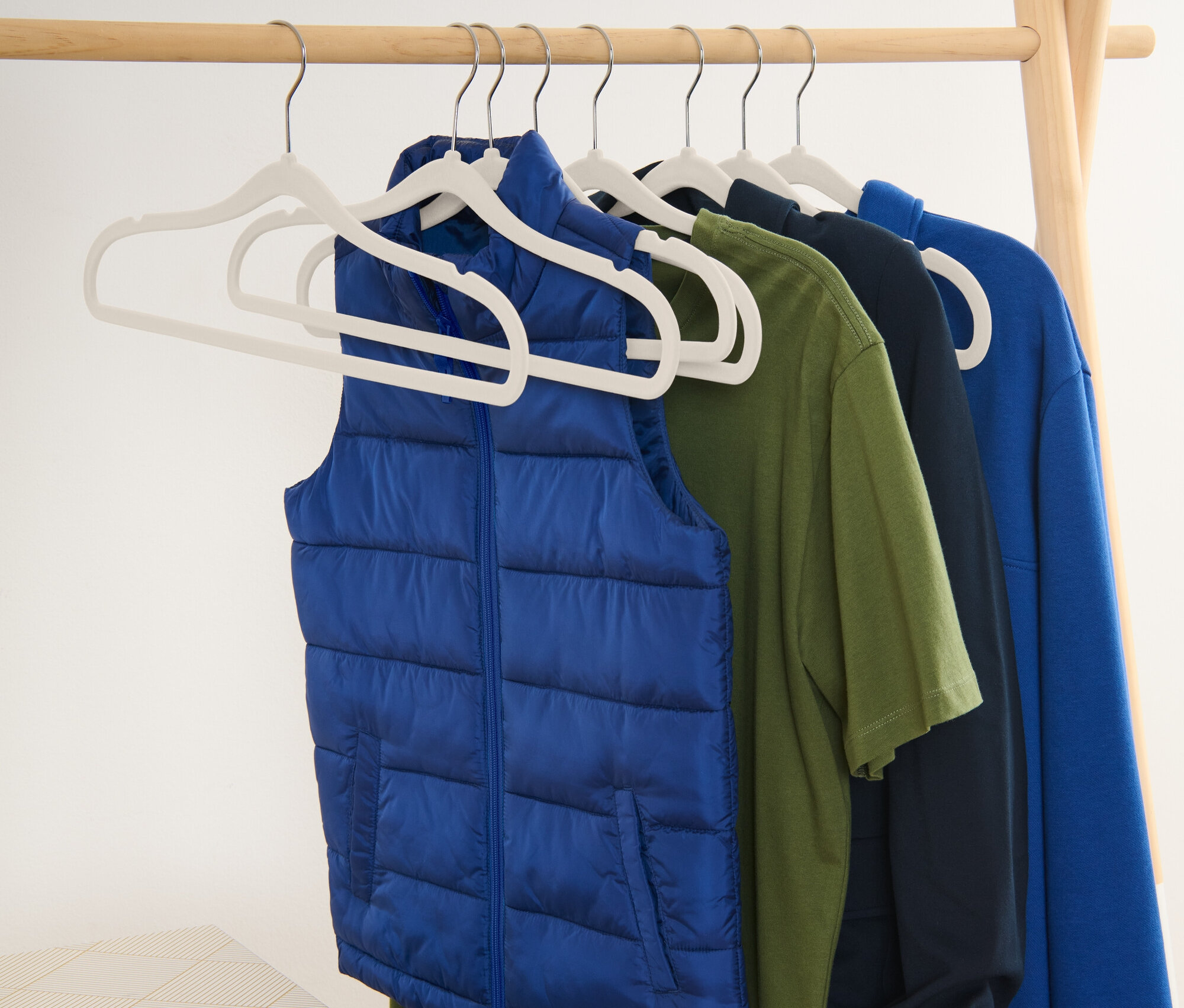 Modrá vesta a tričká visia na vešiakoch na drevenom stojane.