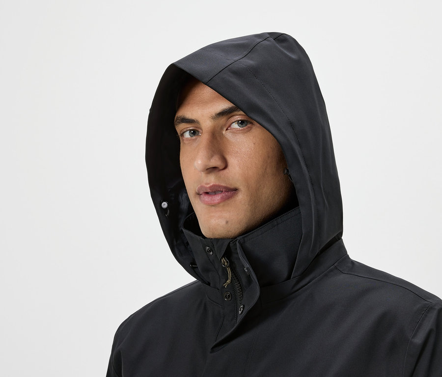 Portrét muža s kapucňou čiernej bundy na svetlom pozadí.