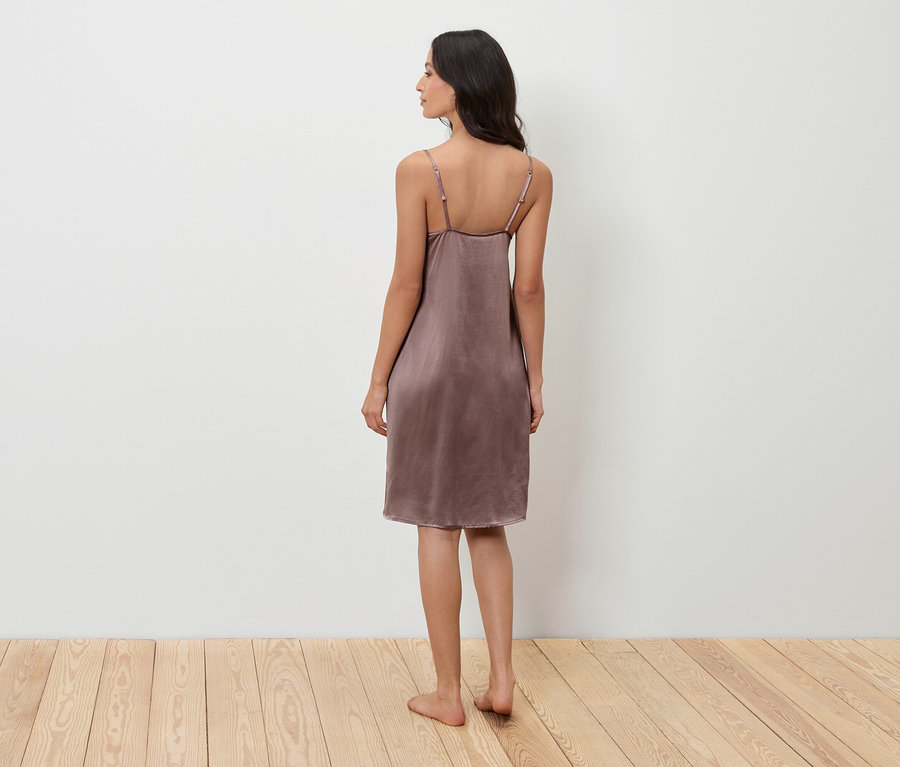 Žena stojí chrbtom k fotoaparátu a má na sebe fialovú nočnú košeľu.