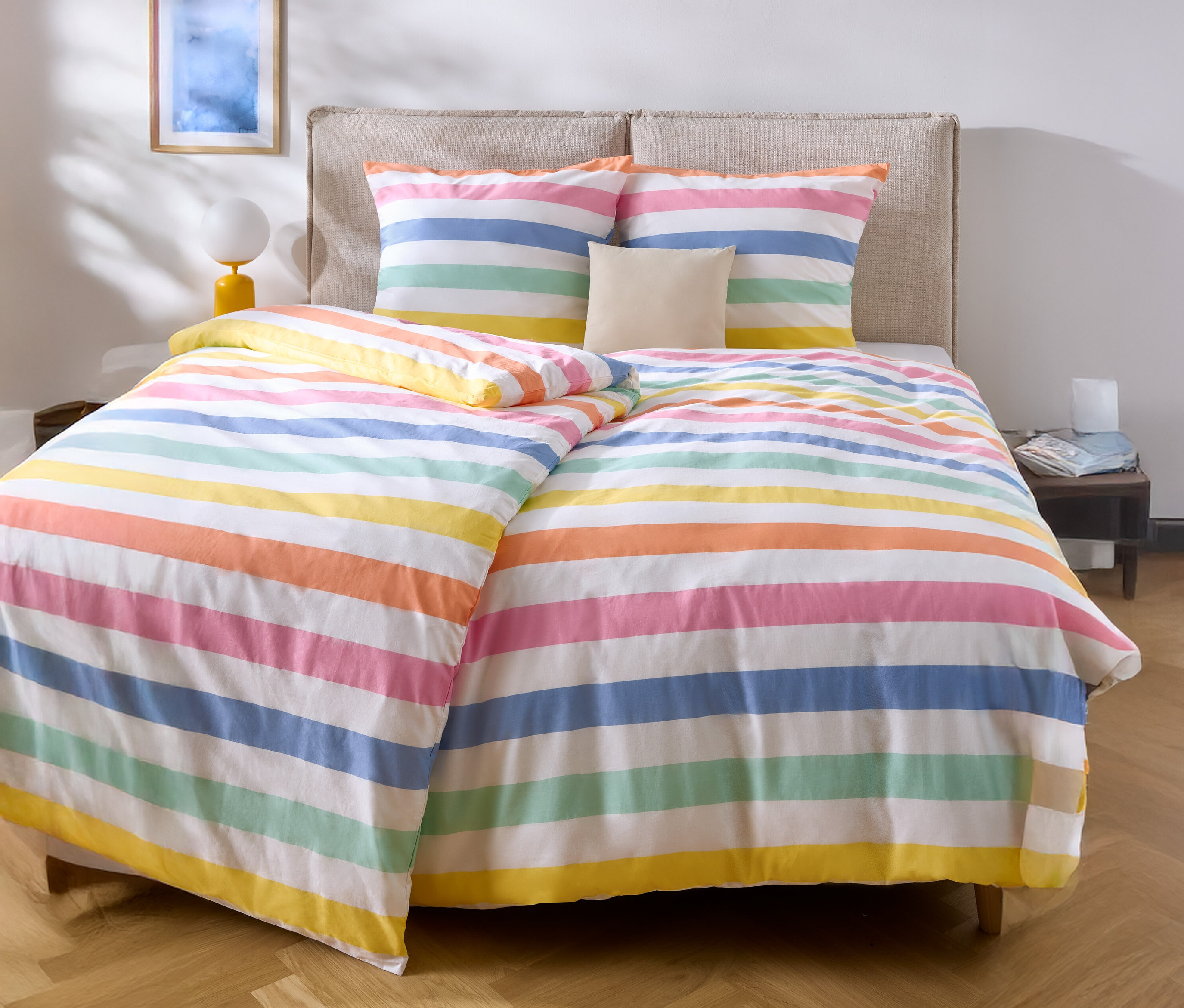 Posteľ s farebnou pruhovanou posteľnou bielizňou a dvoma vankúšmi.