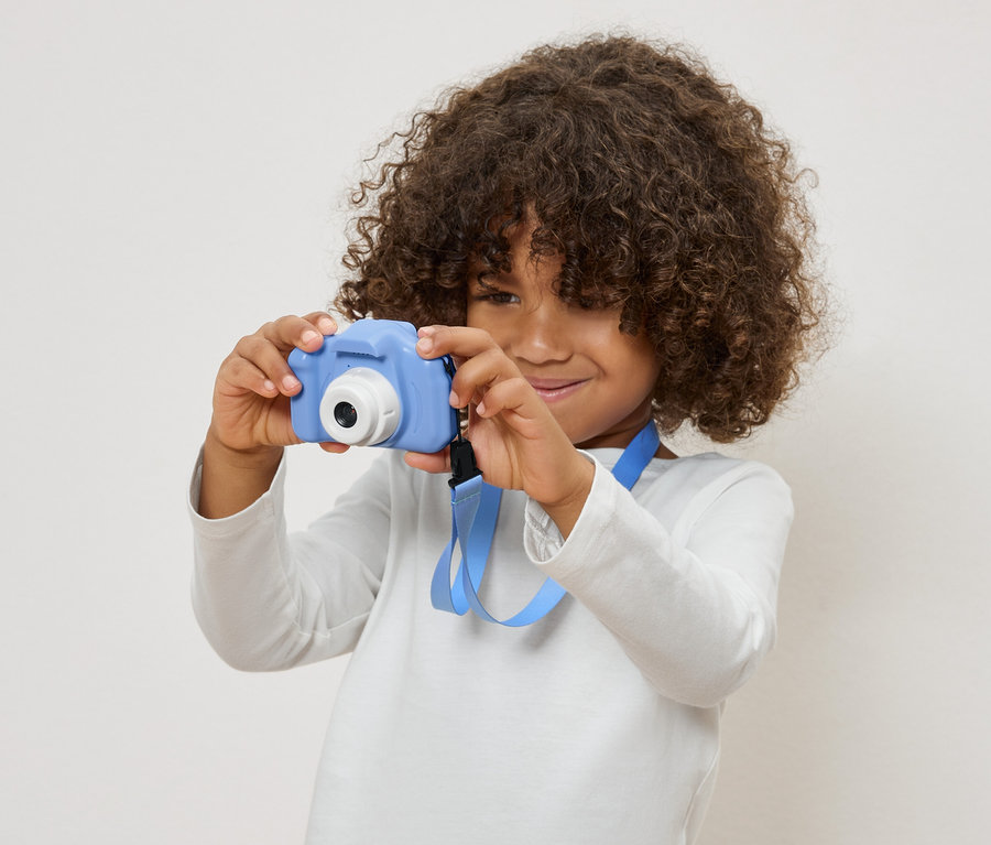 Dieťa s kučeravými vlasmi drží modrý hračkársky fotoaparát.