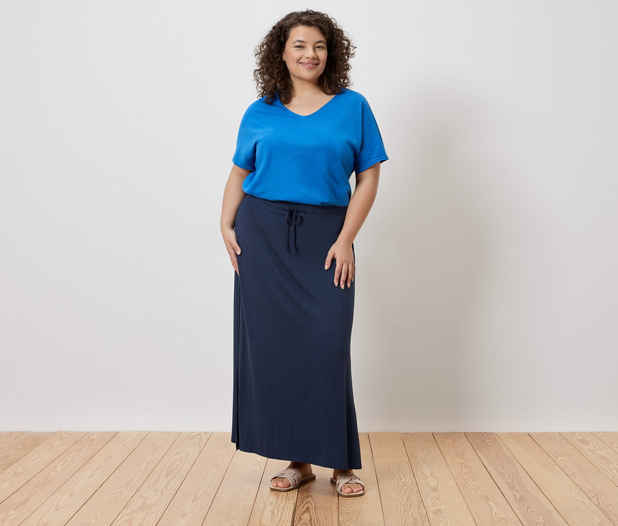 Žena má na sebe modré tričko a dlhú, tmavomodrú sukňu.