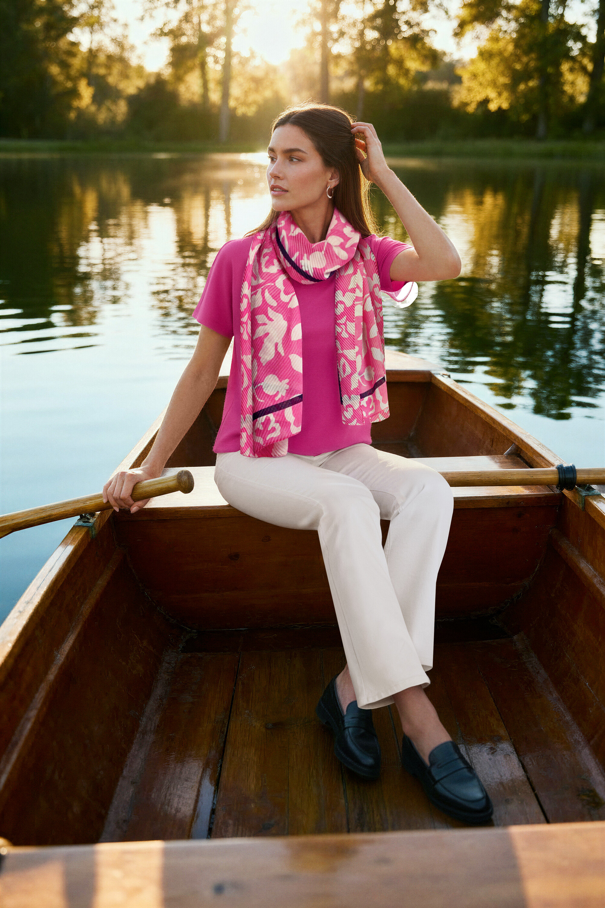 Žena sedí v člne, má na sebe ružovú blúzku, krémové bootcut džínsy ‒ Fit »Lou«, kožené mokasíny a Kruhové náušnice Wave.