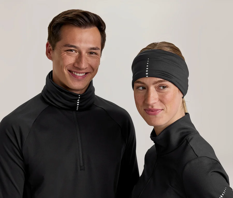 Usmiaty muž a žena v čiernych športových topoch s vysokými goliermi a reflexnými bodkami. Žena má tiež čiernu čelenku s reflexnými bodkami.