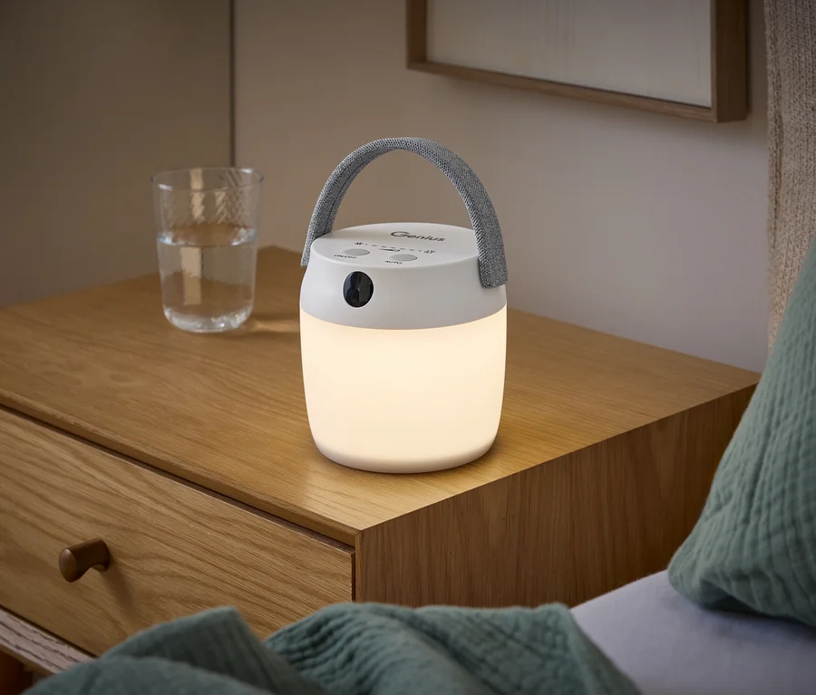 Biela LED lampa so sivou rúčkou svieti na drevenom nočnom stolíku vedľa pohára vody.