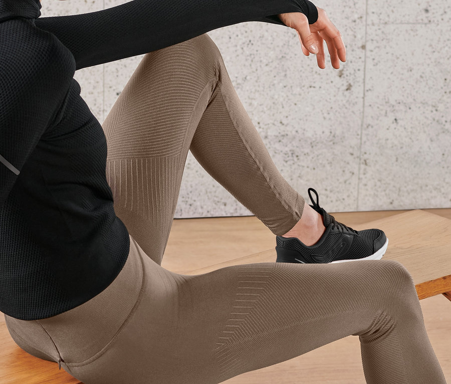 Žena sedí na lavičke a má na sebe prémiové bezšvové bežecké legínsy a čierne tenisky.