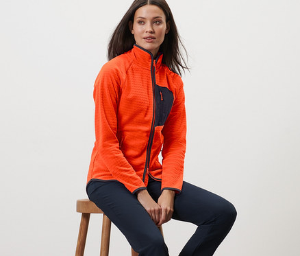 Žena sedí na stoličke a má na sebe flaušovú mikinu.