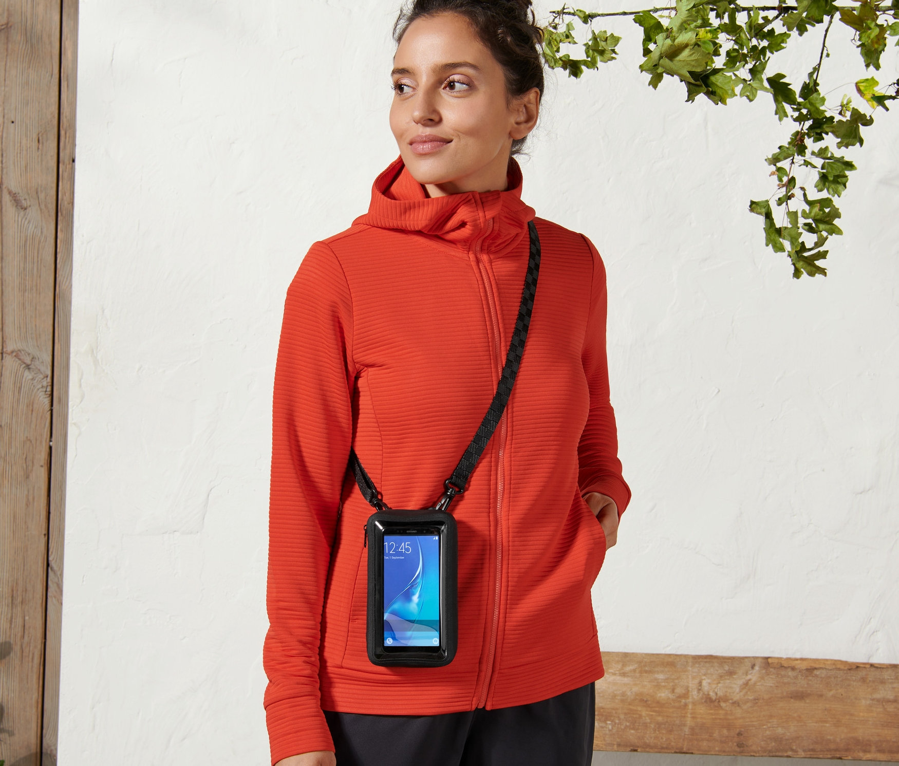 Žena nosí kapsičku 2 v 1 na smartfón s čiernym popruhom cez telo.