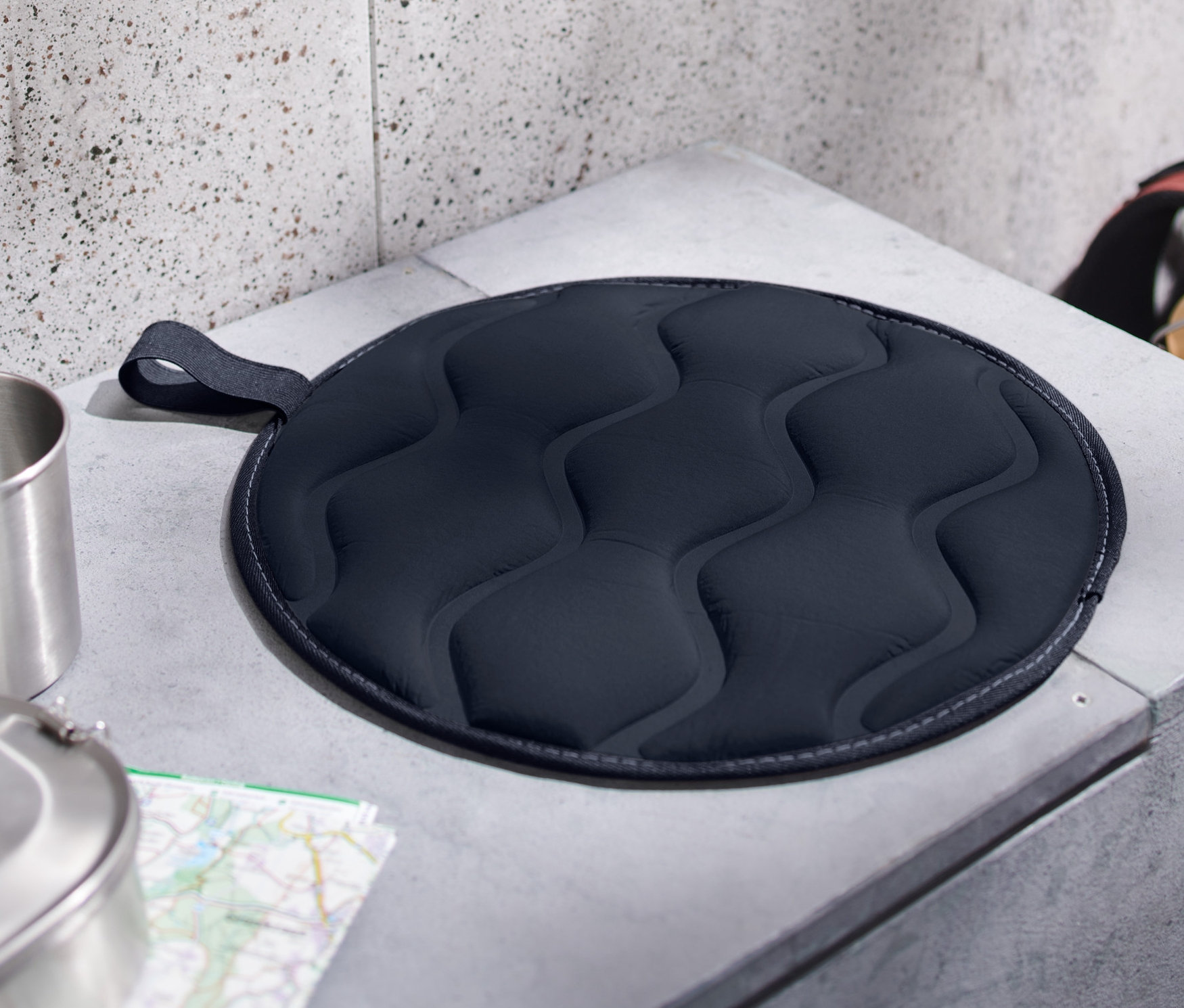 Na sivej betónovej lavičke leží zložený termovankúš na sedenie.