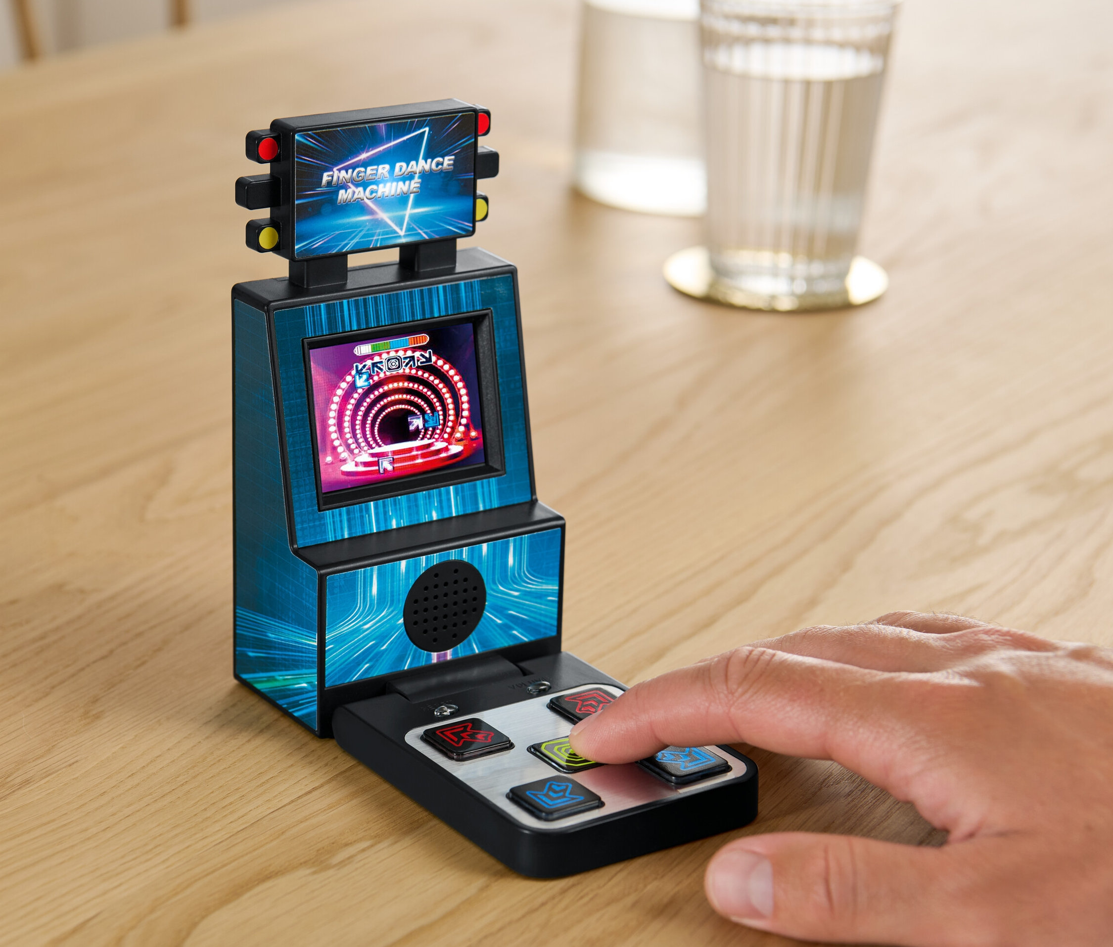 Ruka hrá na Prstovom tanečnom stroji na stole vedľa pohára vody.