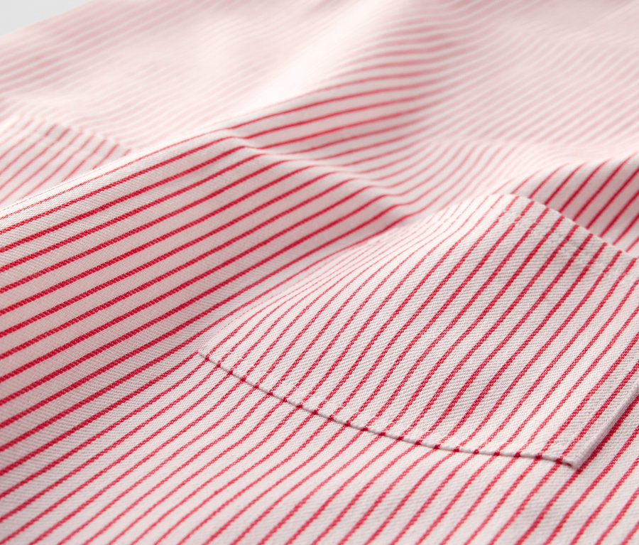 Detail detských tkaných pinaforových šiat s červenými prúžkami a vreckom.