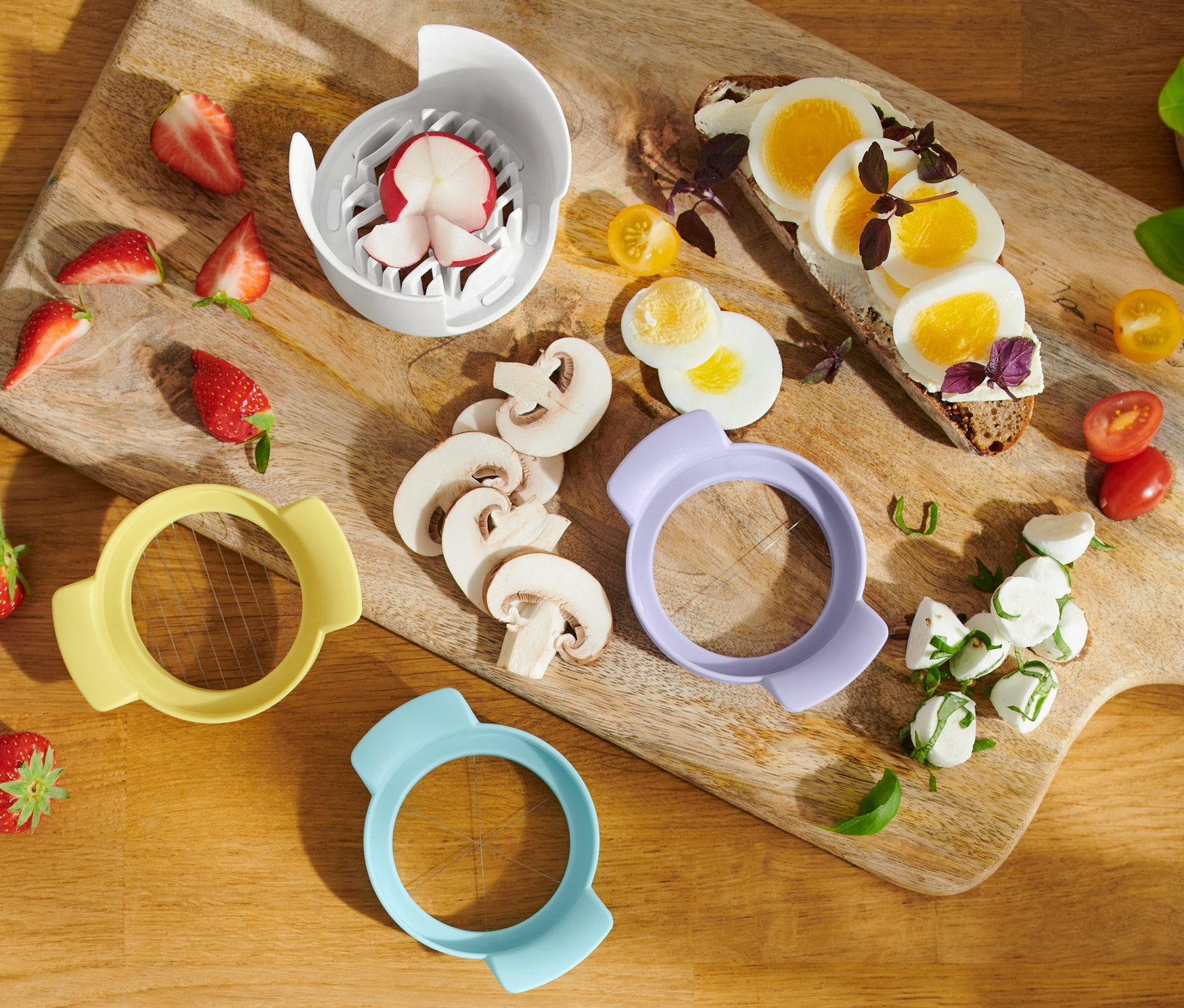 Na drevenej doske sú jahody, huby, krájač na vajíčka 3 v 1, toast s vajíčkom, mozzarella a cherry paradajky.