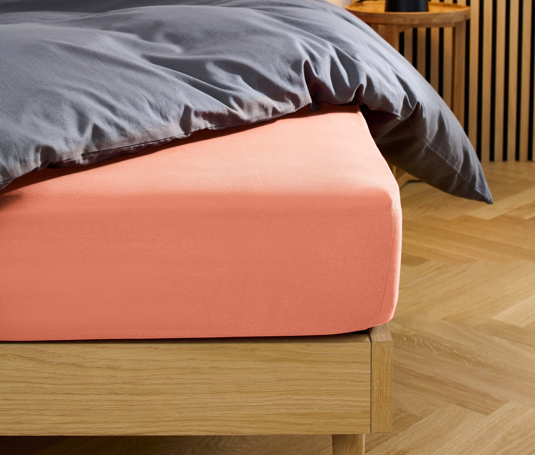 Posteľ s koralovou džersejovou napínacou plachtou.