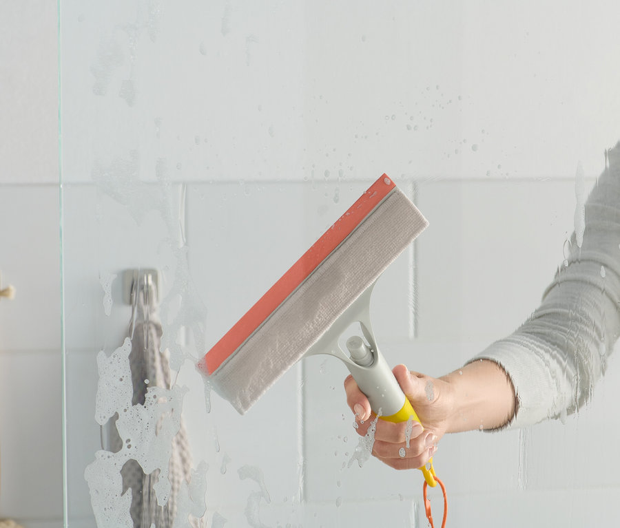 Žena používa stierku na okná 3 v 1 na sklenenú sprchovú zástenku.