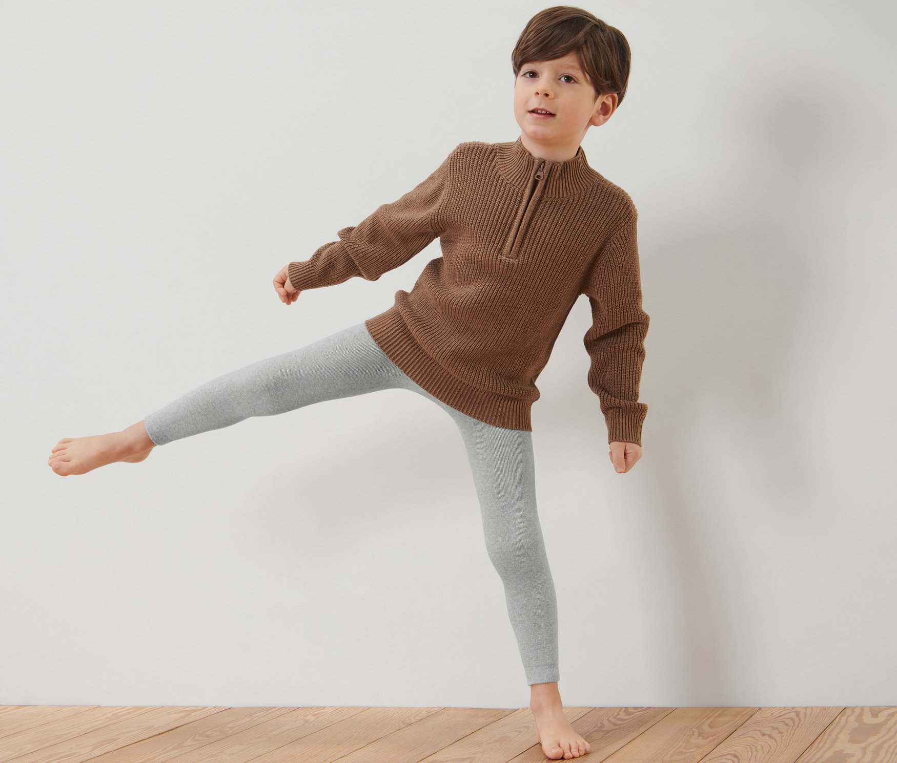 Chlapec stojí na drevenej podlahe a má na sebe hnedý sveter a modro-sivé detské termo legínsy, 3 ks.