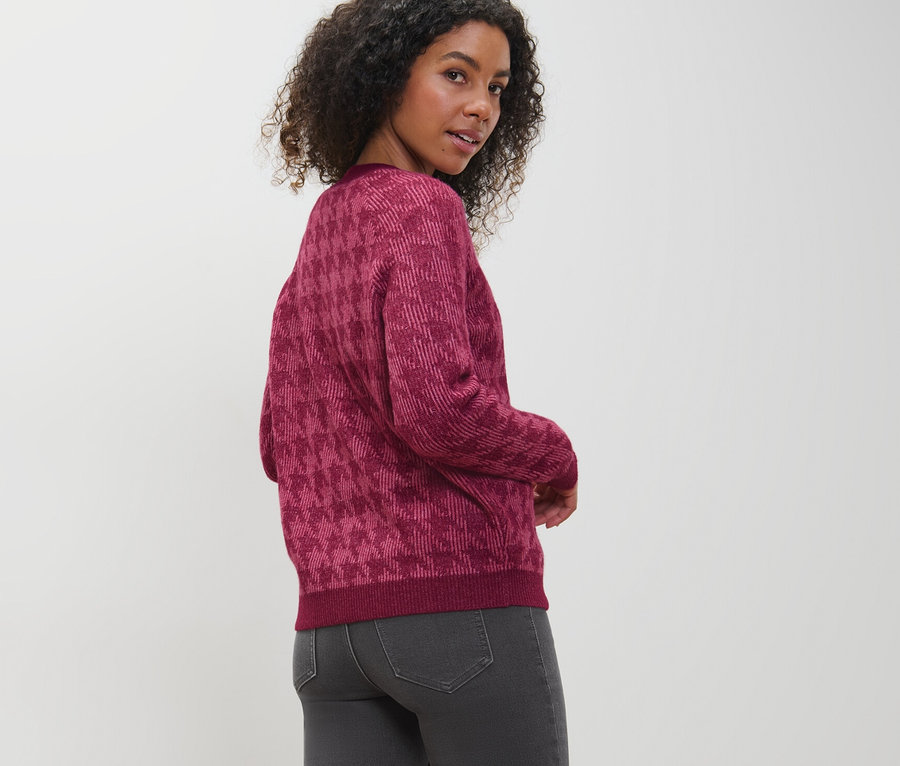 Žena sa pozerá cez plece a má na sebe kardigán z hrubého úpletu so žakárovým vzorom kohútej stopy.