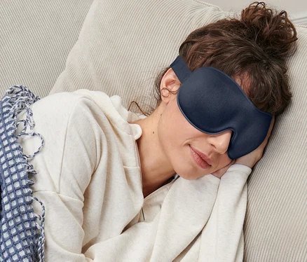 Žena spí na gauči s maskou na spanie.