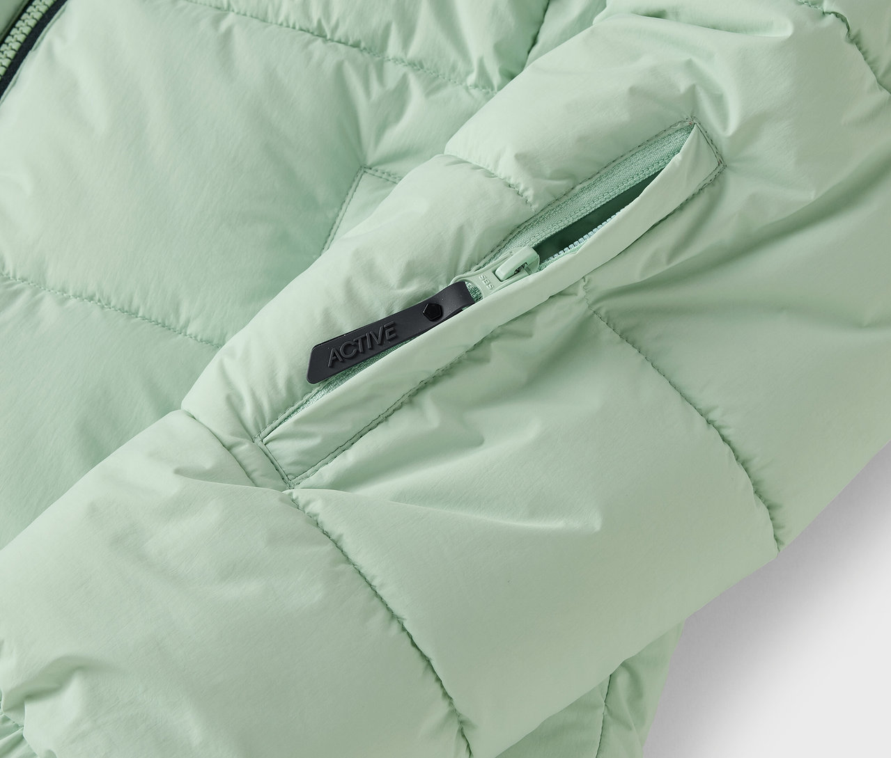 Detail svetlozelenej prešívanej bundy s vreckom na zips.