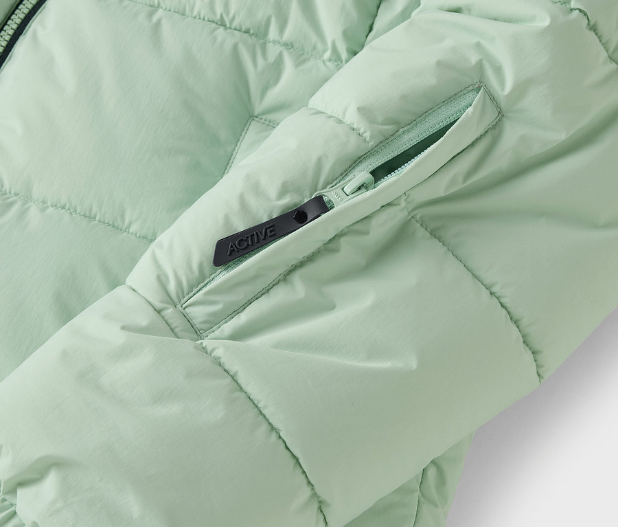 Detail svetlozelenej prešívanej bundy s vreckom na zips.