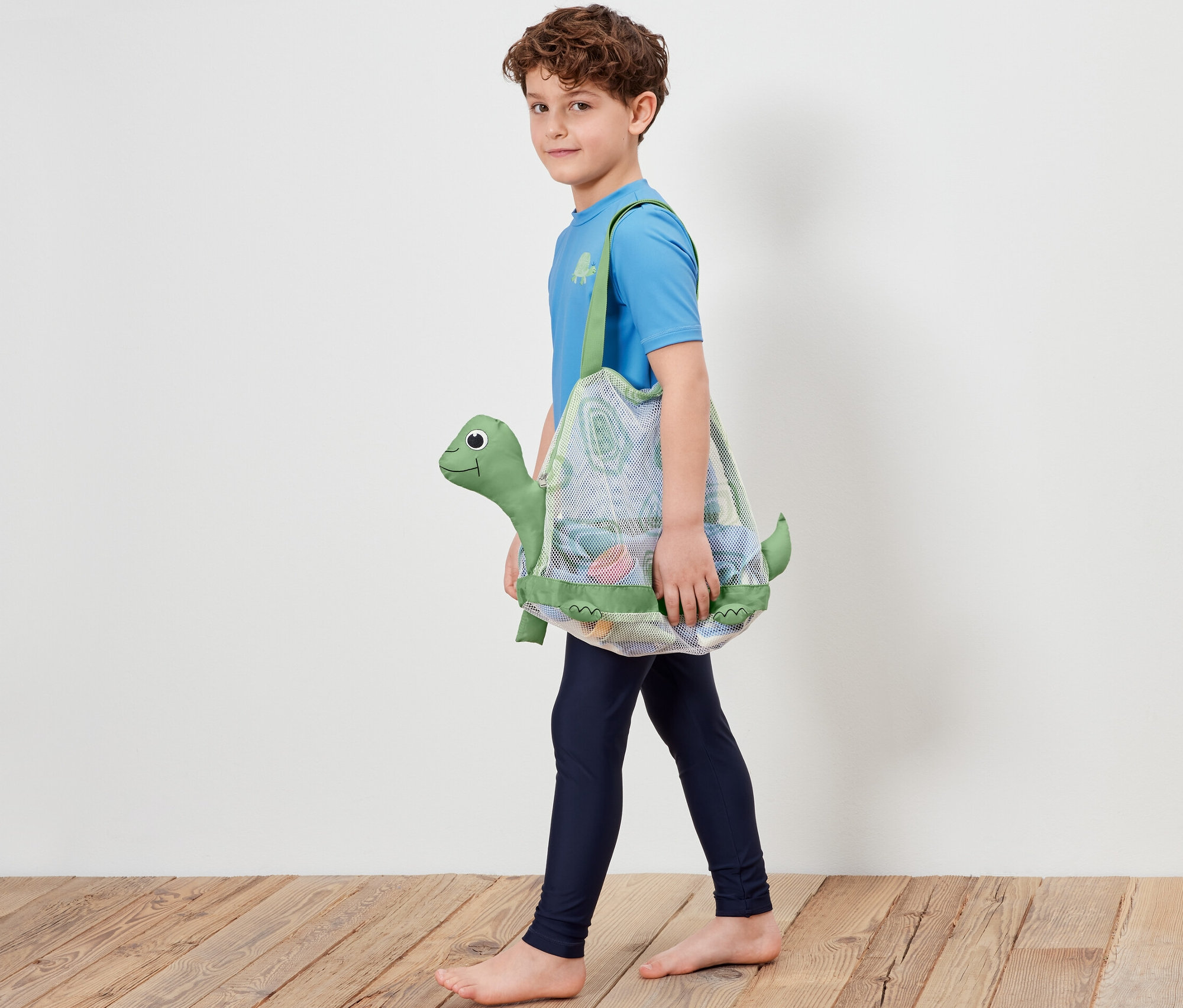 Chlapec kráča a nesie sieťovú tašku na plážové hračky s motívom korytnačky.
