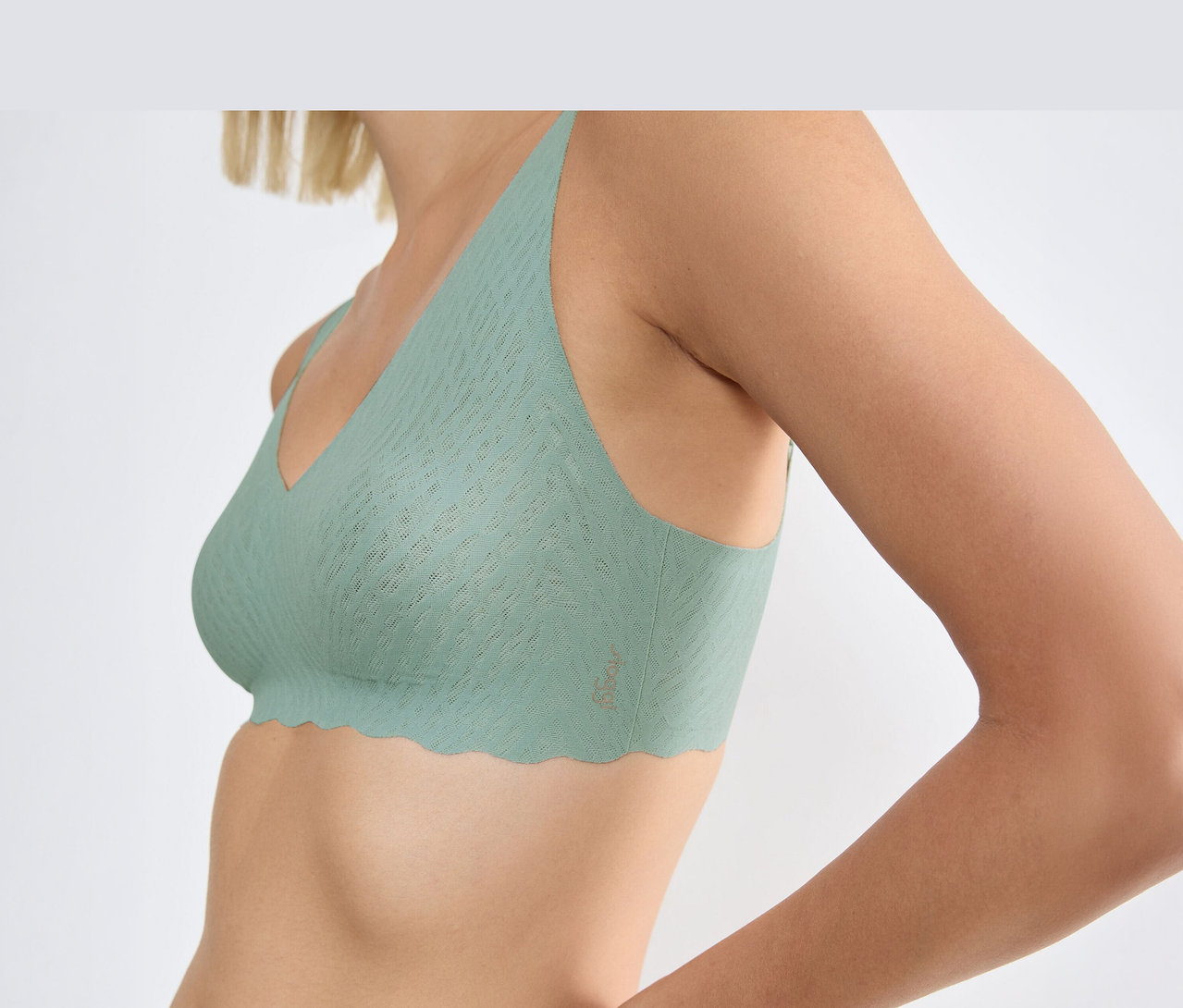 Žena má na sebe svetlozelenú podprsenku sloggi ZERO Feel Bliss Soft Bra v odtieni misty turquoise s vlnitým lemom a textúrovaným vzorom.