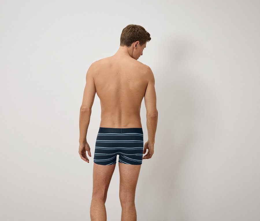 Muž chrbtom ku kamere má na sebe modré pruhované boxerky.