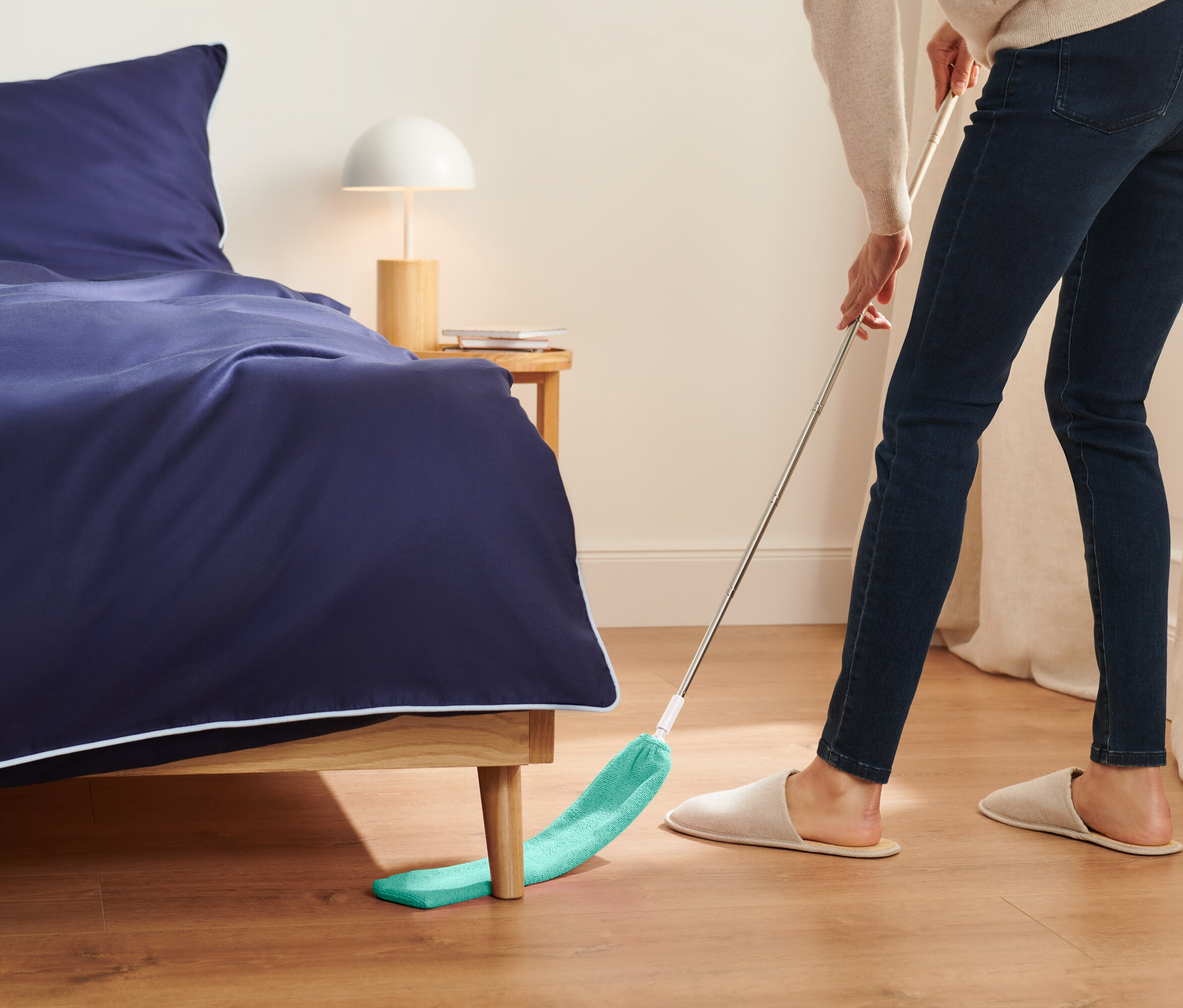 Žena vytiera podlahu pod posteľou zeleným mopom.