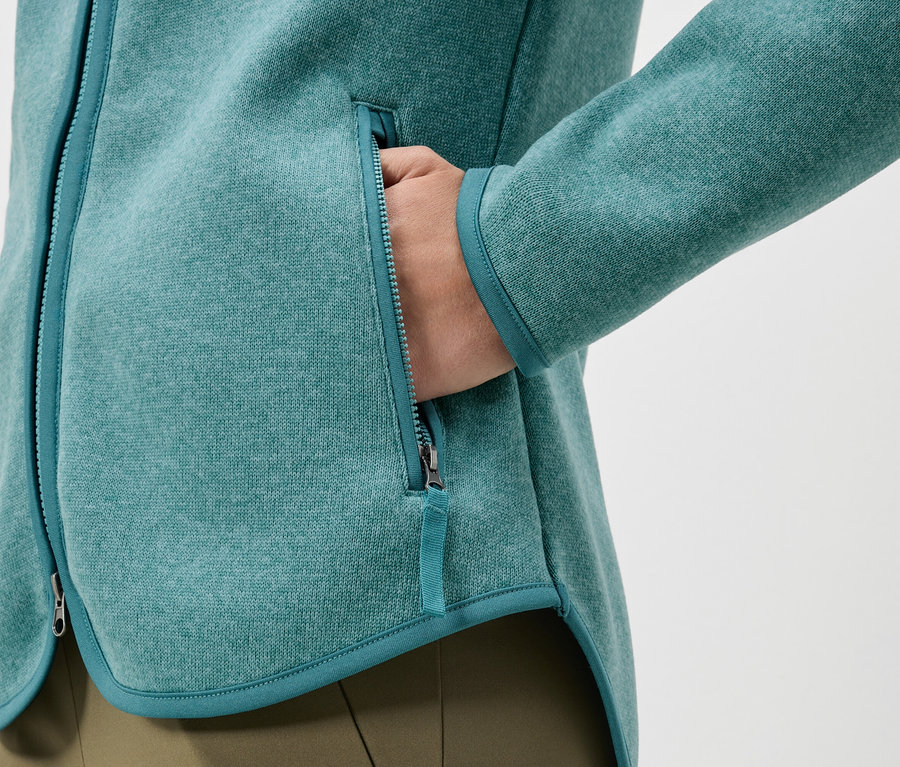 Detailný záber tyrkysovej fleecovej bundy s rukou vo vrecku.
