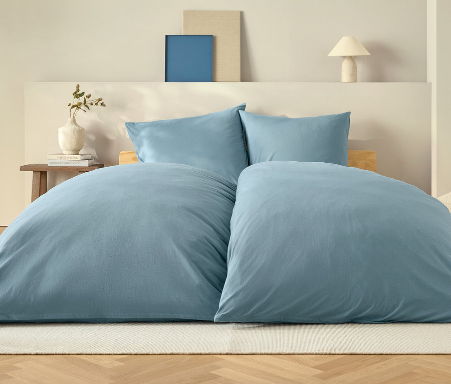 Modrá prikrývka a dva vankúše na posteli na bielom koberci.