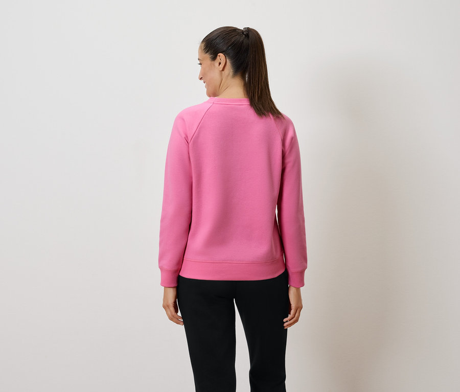 Žena v ružovej mikine a čiernych nohaviciach stojí chrbtom k fotoaparátu.