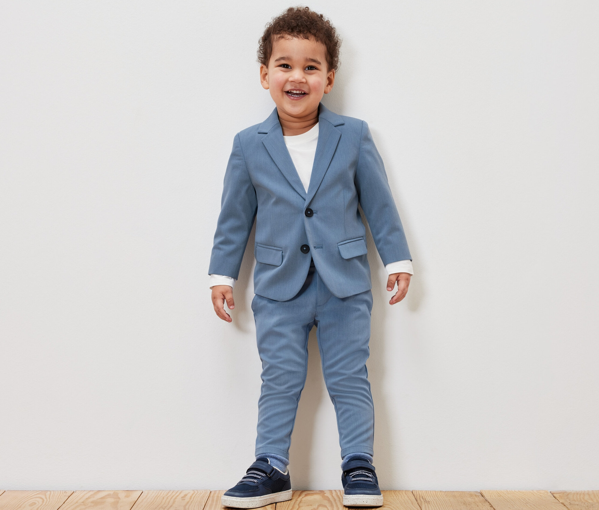 Usmievajúci sa chlapček v detskom saku a chino nohaviciach modrej farby.