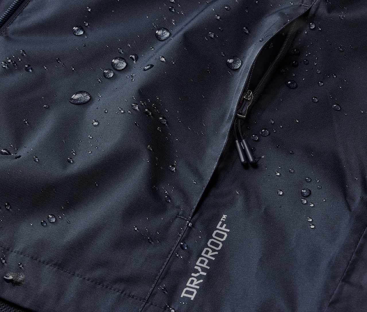 Detail námorníckej modrej bundy do dažďa s vreckom na zips a nápisom DRYPROOF.