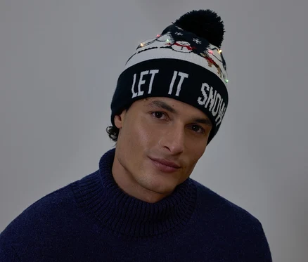 Portrét muža s vianočnou čiapkou s nápisom LET IT SNOW a malými svetielkami.