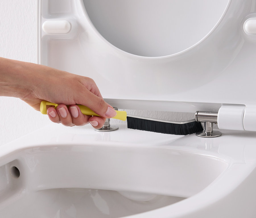 Ruka čistí biely záchod žltou kefou.