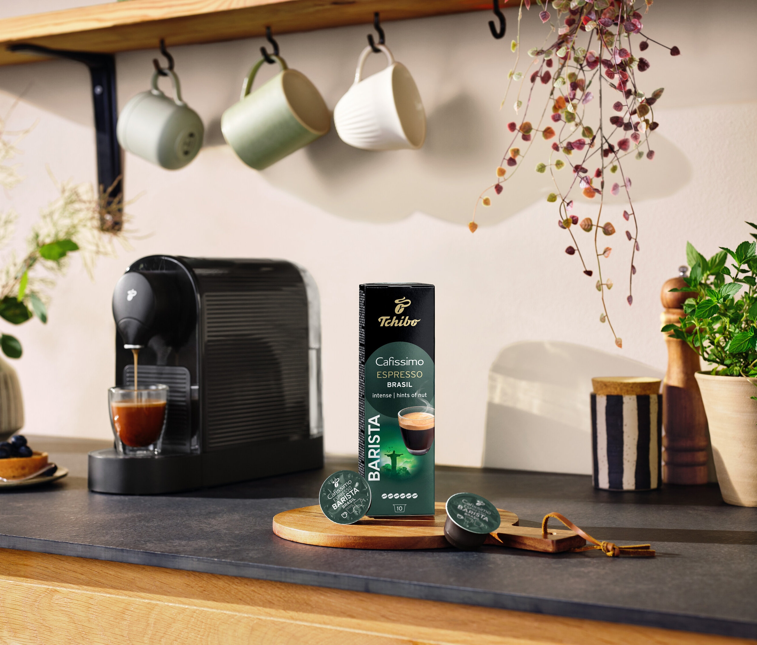 Čierny kávovar pripravuje kávu do pohára vedľa balenia kapsúl Espresso Brasil – 10 kapsúl.