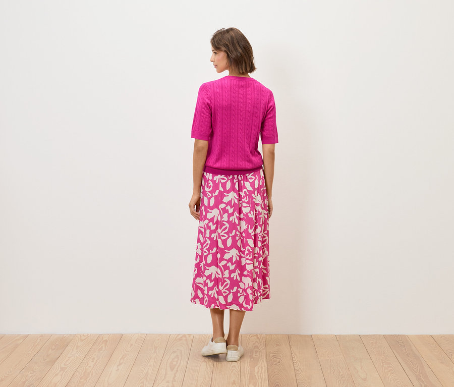 Žena stojí chrbtom, má na sebe ružový top a sukňu s kvetinovým vzorom.