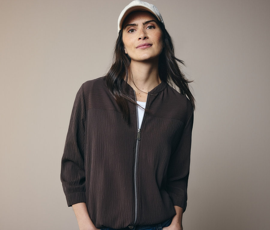 Žena v hnedej bunde a bielej šiltovke.