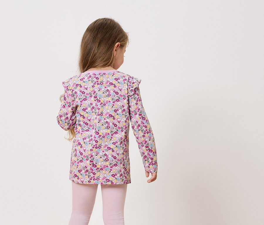 Pohľad zozadu na malé dievča s dlhými vlasmi v blúzke s dlhými rukávmi s kvetinovou potlačou a ružových legínach.