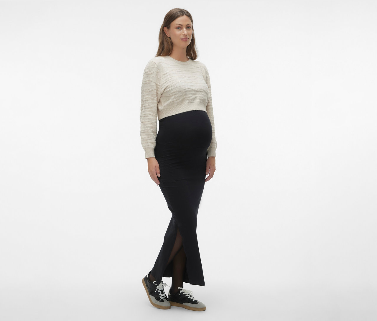 Žena má na sebe čiernu maxi sukňu MAMALICIOUS »MLEMMA TUBE«, svetlý sveter a tenisky.